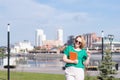 A happy young blonde student girl in sunglasses walking along a city street, carries an orange digital tablet.