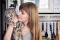 Happy young blonde woman in casual t-shirt holding gorgeous scottish fold cat at domestic kitchen. Natural window light portrait. Royalty Free Stock Photo