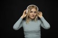 Happy young blonde woman girl listening music in white headphones and look in camera on black background. Charming girl Royalty Free Stock Photo