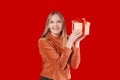 Happy young blonde woman 20s wears green denim jacket hold shake red present box with gift ribbon bow try to guess what