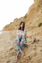 Happy young boho woman sitting and relaxing on sunny beach with rock. Hipster bohemian carefree girl smiling at sea. Summer Royalty Free Stock Photo