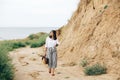 Happy young boho woman in white shirt walking on tropical island at sandy cliff and grass. Stylish hipster girl relaxing on beach Royalty Free Stock Photo