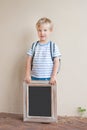 A happy young boy with a backpack holding a chalkboard against a