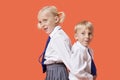 Happy young boy and girl in school uniform standing back to back over orange background Royalty Free Stock Photo