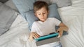 Happy young boy is playing with a tablet computer while lying in bed during the day. Child using gadget, education and development Royalty Free Stock Photo