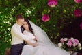 Happy young bride and groom in a pink decorated with peonies area in nature, family, relationships, romance, smiles, hugs, love Royalty Free Stock Photo