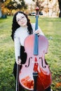 Happy young brunette woman with glasses smiling and playing cello at sunset in the park. Vertical. Royalty Free Stock Photo