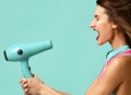 Happy young brunette woman with hair dryer on blue mint background Royalty Free Stock Photo