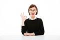 Happy young business lady wearing glasses showing okay gesture.