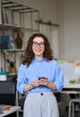 Happy young business woman holding phone standing in office, vertical. Royalty Free Stock Photo