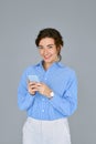 Young happy business woman holding mobile phone standing at gray wall. Royalty Free Stock Photo