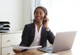 Happy young business woman sitting at office desk talking on mobile phone with a document in hand
