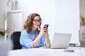 Happy young business woman using cellphone working in office sitting at desk. Royalty Free Stock Photo