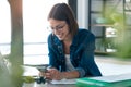 Happy young business woman using her mobile phone while working with computer in the kitchen at home Royalty Free Stock Photo