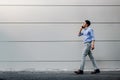 Happy Young Businessman in Casual wear Using Mobile Phone while Walking by the Urban Building Wall. Lifestyle of Modern People. Royalty Free Stock Photo