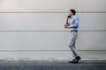 Happy Young Businessman in Casual wear Using Mobile Phone while Walking by the Urban Building Wall. Lifestyle of Modern People. Royalty Free Stock Photo