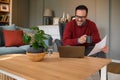 Happy young businessman holding coffee cup and document discussing over video call on laptop at home Royalty Free Stock Photo