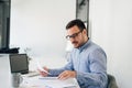 Happy young businessman looking at papers graphs and charts using laptop at his office desk Royalty Free Stock Photo