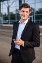 Happy young businessman with mobile phone standing outdoors