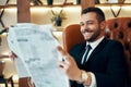 Happy young businessman reading newspaper and latest news while sitting in armchair Royalty Free Stock Photo