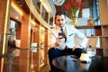 Happy young businessman sitting relaxed on sofa at hotel lobby using smartphone Royalty Free Stock Photo