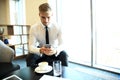 Happy young businessman sitting relaxed on sofa at hotel lobby using smartphone, waiting for someone Royalty Free Stock Photo