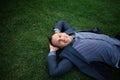 Happy Young businessman in a suit lying on the green grass and relaxing in park. Royalty Free Stock Photo