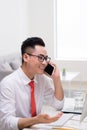 Happy young businessman talking on cell phone and using computer in office Royalty Free Stock Photo