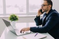 Young businessman talking on cell phone and using laptop in office Royalty Free Stock Photo