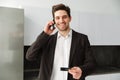 Happy young businessman talking by mobile phone holding credit card. Royalty Free Stock Photo