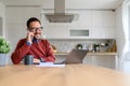 Happy young businessman talking over smart phone while sitting with laptop on desk at home office Royalty Free Stock Photo