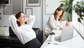 Happy young businesswoman relaxing hands behind head sitting at desk with laptop in shared office, panorama Royalty Free Stock Photo