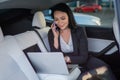 Happy young businesswoman typing at laptop and talking on smartphone while sitting on the back seat of car. Working Royalty Free Stock Photo