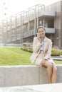 Happy young businesswoman using mobile phone while sitting on wall against office building Royalty Free Stock Photo