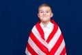 Happy young caucasian american boy kid child schoolboy wraps himself in a U.S. flag and look at camera Royalty Free Stock Photo