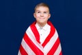 Happy young caucasian american boy kid child schoolboy wraps himself in a U.S. flag and look at camera Royalty Free Stock Photo