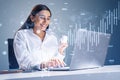 Happy young caucasian businesswoman with coffee cup sitting at desk and using laptop with growing blue forex chart and map Royalty Free Stock Photo