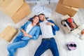 Happy young caucasian couple lying down on the wooden floor while having a break while moving to new house. Top view. Royalty Free Stock Photo