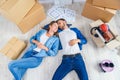 Happy young caucasian couple lying down on the wooden floor while having a break while moving to new house. Top view. Royalty Free Stock Photo