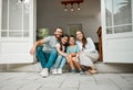 Happy young caucasian family of four sitting at their front door smiling and looking at the camera. Two parents sitting Royalty Free Stock Photo