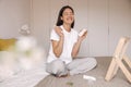 Happy young caucasian girl sitting on bed and rejoices in her new skin care creams at home. Royalty Free Stock Photo