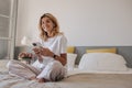 Happy young caucasian girl with smart watch sitting on bed using her smartphone home. Royalty Free Stock Photo