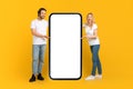 Happy young caucasian male and female in white t-shirts presentation huge phone with empty screen