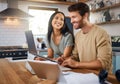 Happy young caucasian man working on laptop in the kitchen at home while his wife stands next to him and smiles while he Royalty Free Stock Photo