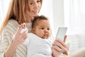 Happy young caucasian mother holding cute african baby daughter using phone. Royalty Free Stock Photo