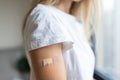 Happy young caucasian woman with blonde hair in white t-shirt showing patch on arm, feeling good after anti coronavirus Royalty Free Stock Photo