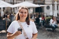 Happy young caucasian woman in good mood walks with coffee around city during day. Lifestyle concept. 30s girl holding Royalty Free Stock Photo
