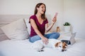 Happy young caucasian woman at home working on laptop and mobile phone while cute jack russell dog resting on bed during daytime. Royalty Free Stock Photo