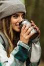 Happy young caucasian woman in jacket in forest drinks cup of tea, enjoy travel, vacation and hot coffee