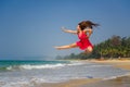 Happy young caucasian woman jumping high above wet sand in tropical sea on sunny day. Barefoot, a sporty girl in short red dress Royalty Free Stock Photo